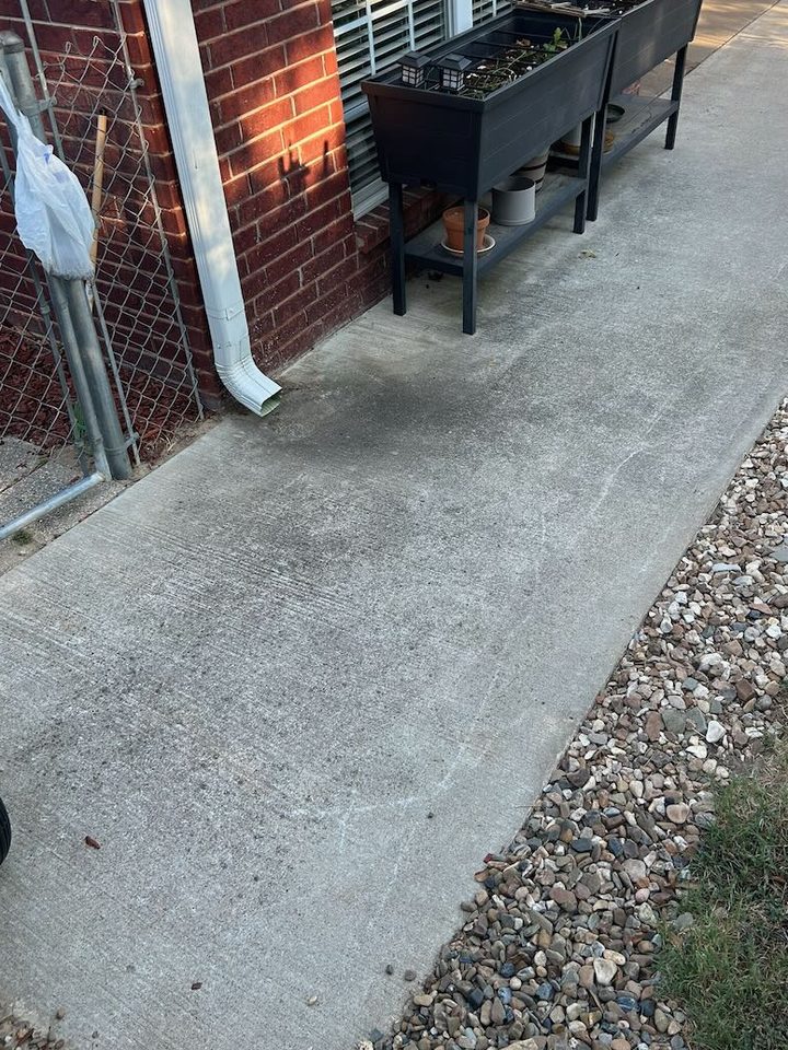 Concrete walk beside a brick home, darkened with mildew below the downspout and around a planter, before cleaning